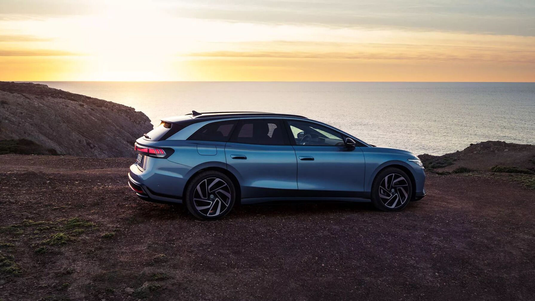 Der VW ID.7 Tourer steht im Sonnenuntergang mit Blick auf das Meer und zeigt seine elegante, langgezogene Silhouette.