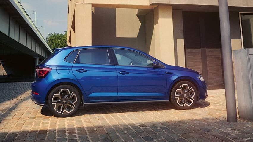 VW Polo steht seitlich vor moderner Gebäudearchitektur. Die klare Linienführung und die sportlichen Felgen unterstreichen die solide Basis dieses kompakten Modells.