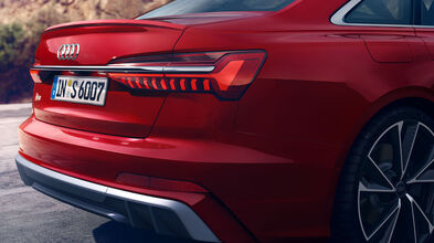 Ein roter Audi S6 Limousine steht, von schräg hinten gezeigt. Auffällig: durchgehendes LED-Leuchtenband, S6-Logo, vier Endrohre, dunkle Scheiben.