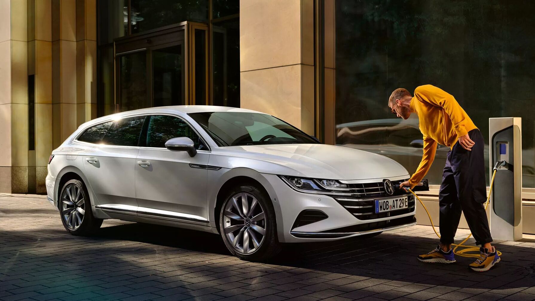 Der weiße VW Arteon Shooting Brake wird an einer Ladesäule vor einem Gebäude geladen. Elegante Linien treffen auf moderne Technik.
