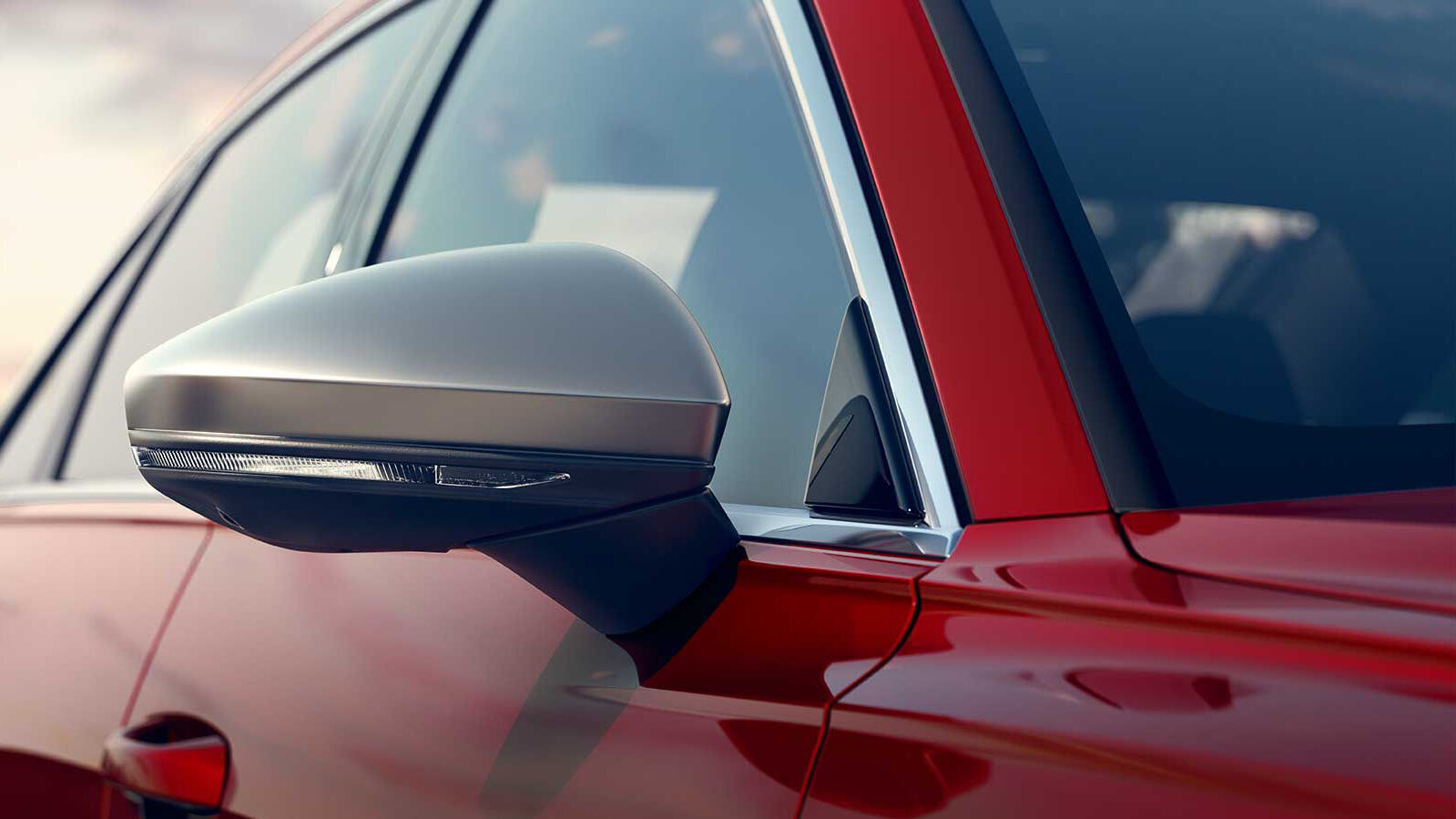 Nahaufnahme eines silbermatten Außenspiegels in Aluminium-Optik mit LED-Blinker, vor roter Tür und dunkler Scheibe.