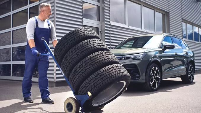 Mechaniker schiebt Autoreifen auf Sackkarre zu geparkten Fahrzeug.