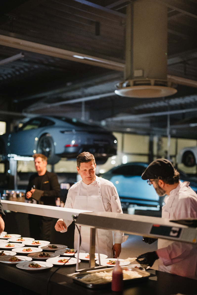 Köche servieren Gerichte in einer Halle mit Sportwagen.
