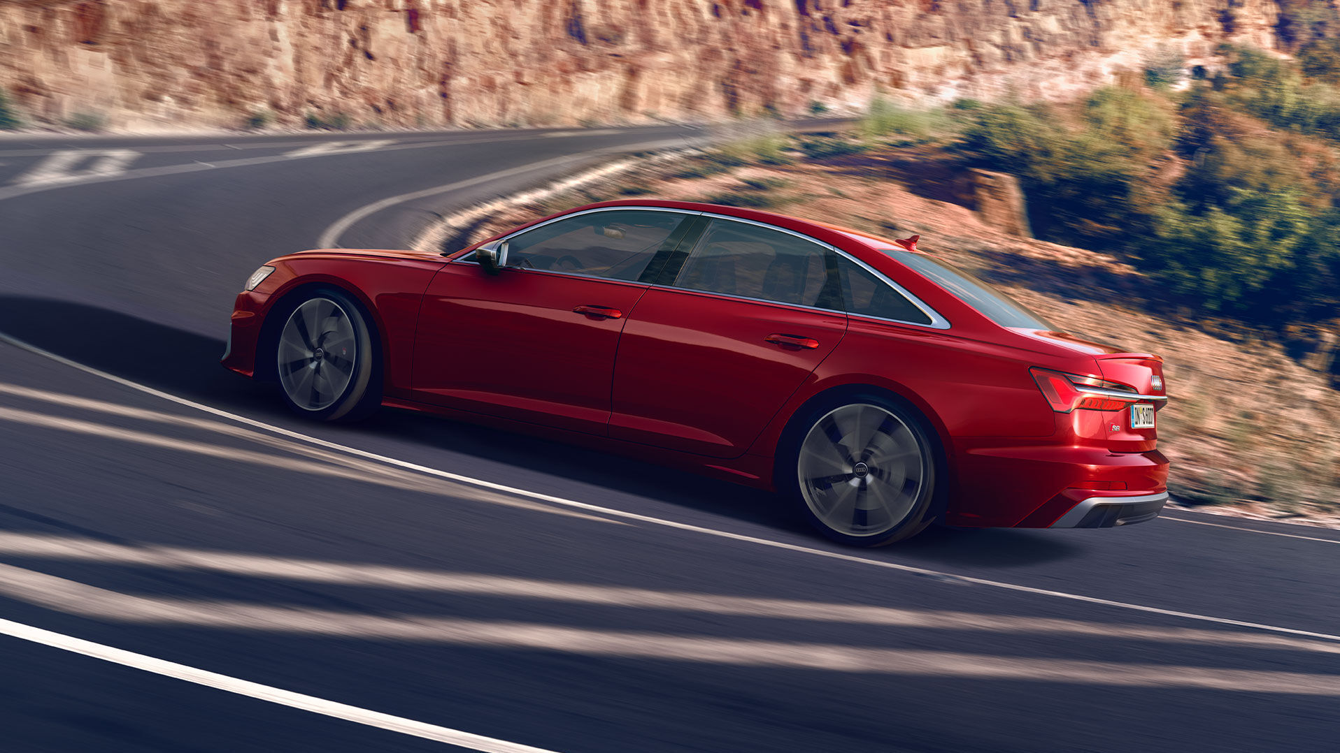 Der Audi S6 Limousine fährt in Rot durch eine Kurve. Sichtbar sind große silberne Felgen, klare Linien und Chrom an den Fenstern.