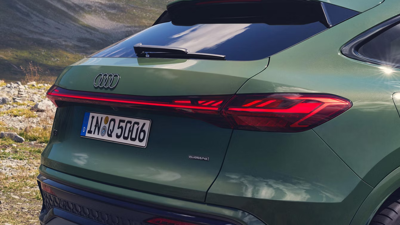 Audi Q5 Sportback in Distriktgrün Metallic fährt durch Berge mit digitalen OLED-Rückleuchten und LED-Lichtband.