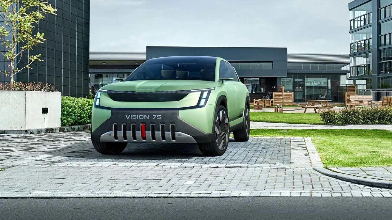 Der Vision 7S steht vor moderner Architektur und zeigt seine klare Designsprache mit markanter Front. Das Fahrzeug wirkt modern solide.