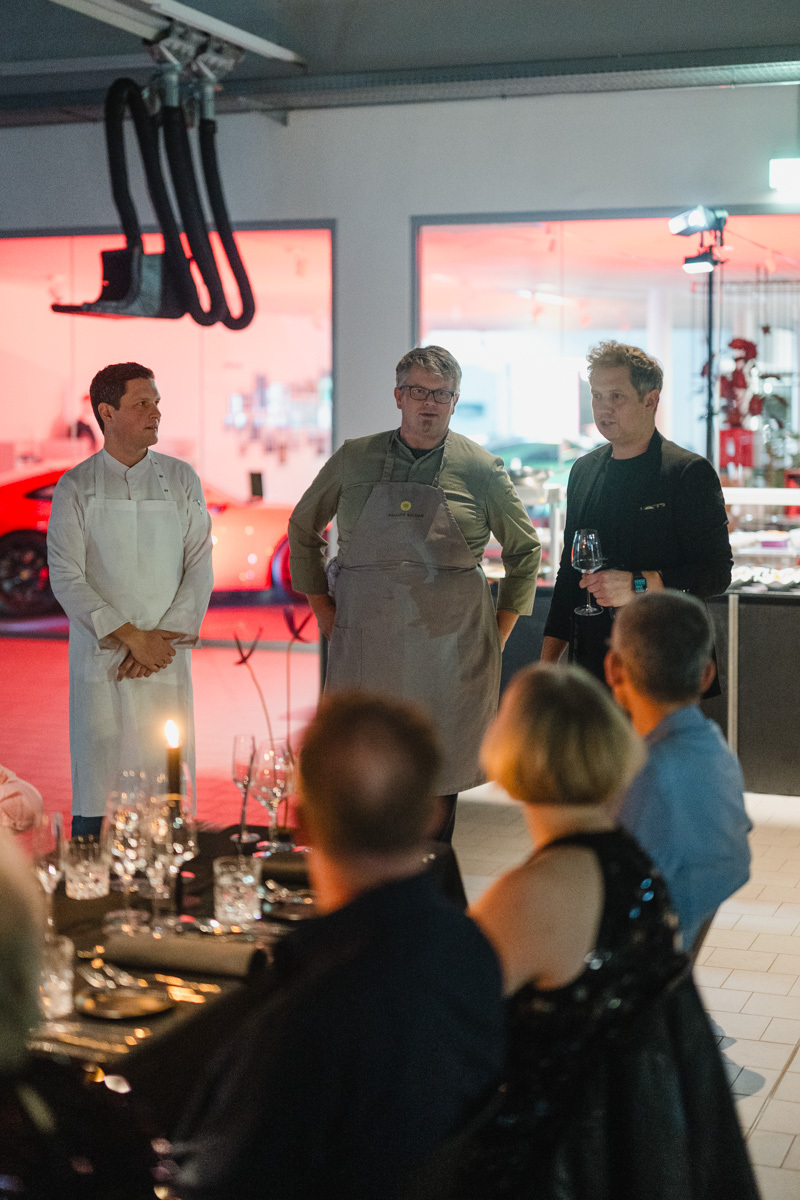 Köche servieren Gerichte in einer Halle mit Sportwagen.