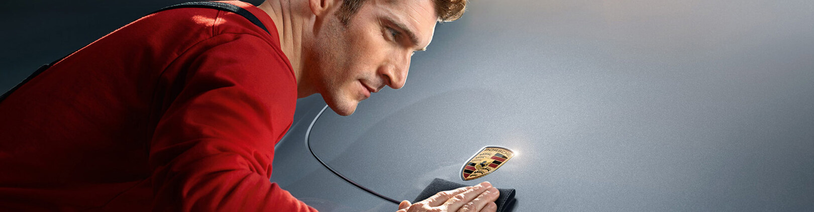 Mann poliert Motorhaube mit Porsche Emblem
