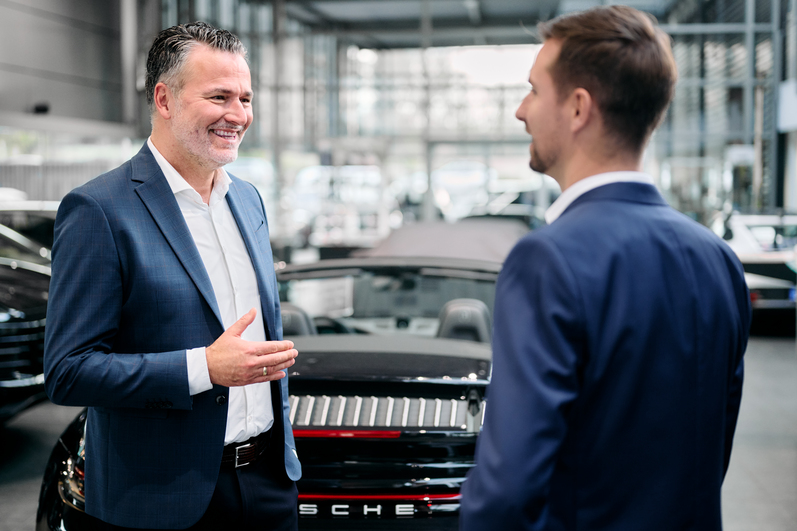 Zwei Verkaufsberater im Porsche Zentrum geben sich die Hand vor einem Porsche 911 Carrera Cabriolet